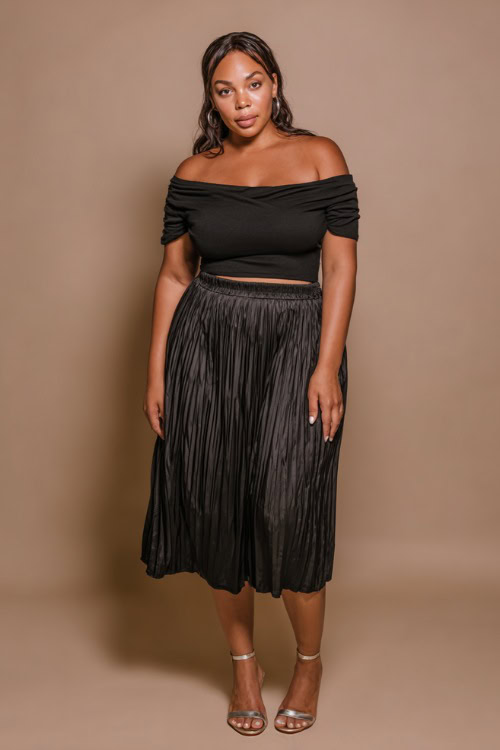 A plus-size woman wearing a fitted black off-shoulder top with a pleated midi skirt and metallic sandals, styled for a casually elegant summer going-out outfit