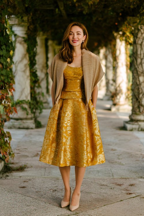A petite woman in a gold jacquard cocktail dress with a fit-and-flare silhouette and cap sleeves, paired with pointed kitten heels and a cashmere wrap