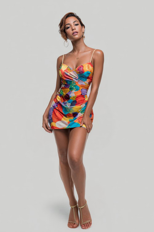 A woman wearing a colorful abstract print mini dress with thin straps and gold sandals, perfect for a fun summer night at the club, simple studio background