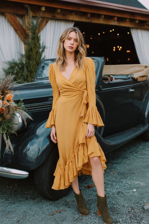 A woman wears a marigold wrap dress with flared sleeves and a ruffle hem, styled with dark olive ankle boots