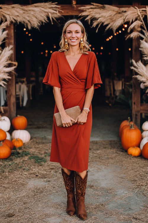 A woman wears a rust wrap midi dress with flutter sleeves and tall brown cowboy boots