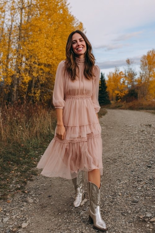 A woman over 30 wearing a blush pink A-line dress with a tiered sheer skirt and high neck, paired with metallic silver cowboy boots