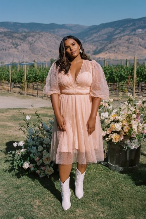 a woman wears a pink wedding guest dress with white cowboy boots for wedding