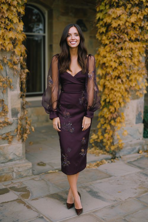 A fashionable guest wears a deep plum midi dress with sheer long sleeves and floral embroidery