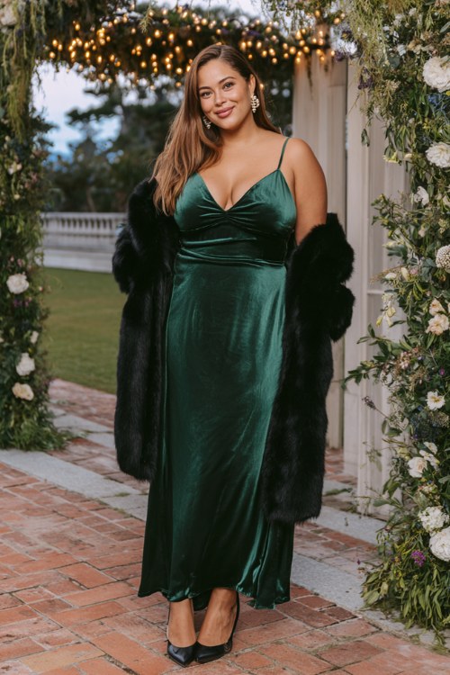 A plus-size woman wears an emerald green velvet gown with a black faux fur coat