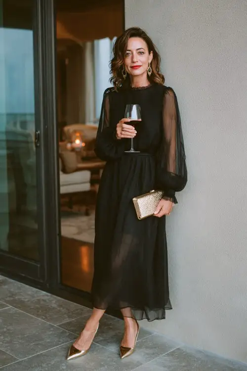 A woman over 40 wears a black chiffon dress with sheer bishop sleeves and a flowy skirt, paired with pointed heels and a metallic clutch