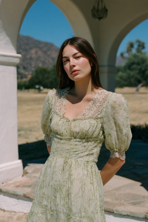 A woman wears a pale sage green dress with a subtle leaf print and lace-trimmed sleeve