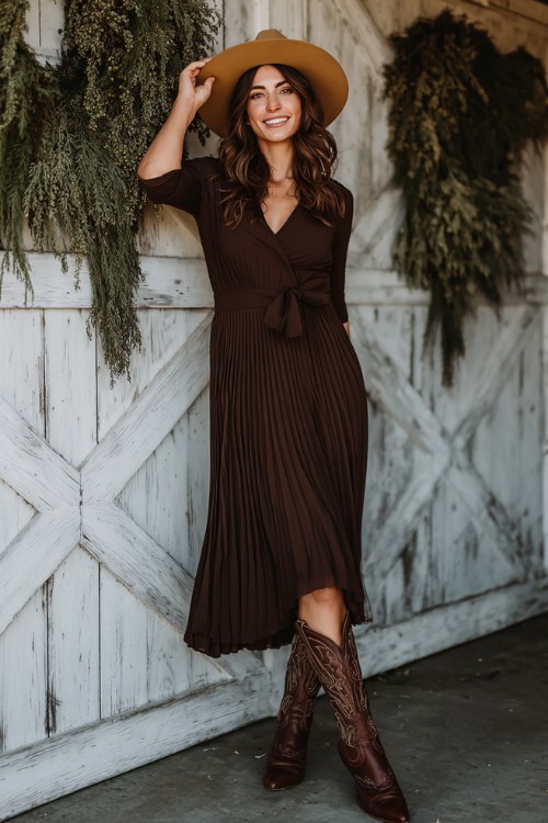 A woman wears a chocolate brown pleated midi dress with tall embroidered cowboy boots