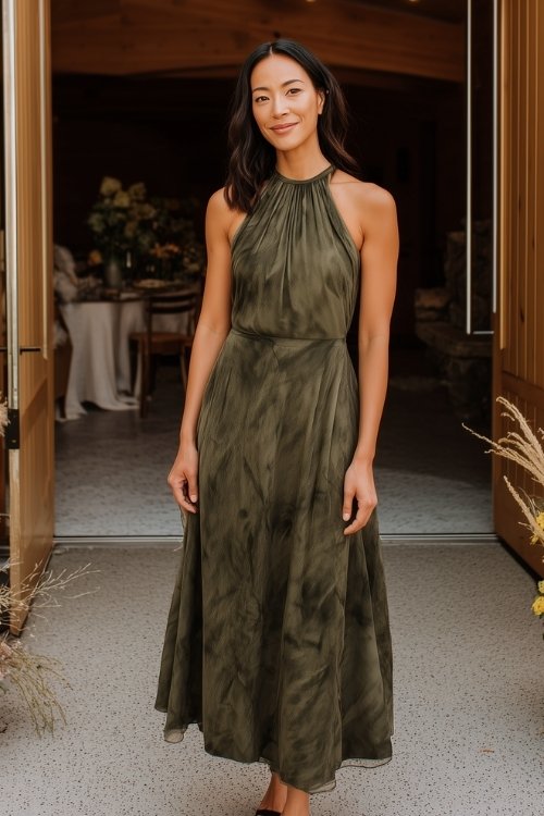 A woman in a moss green painterly-print midi dress with a halter neckline and pleated skirt
