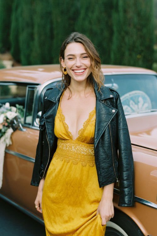 A woman wears a golden mustard wrap dress with lace trim and a cropped leather jacket