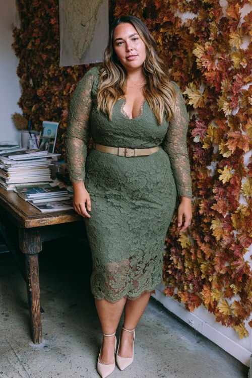 A plus-size woman wears a moss-green cotton-lace midi with scalloped hem and sheer sleeves, styled with cream slingback pumps