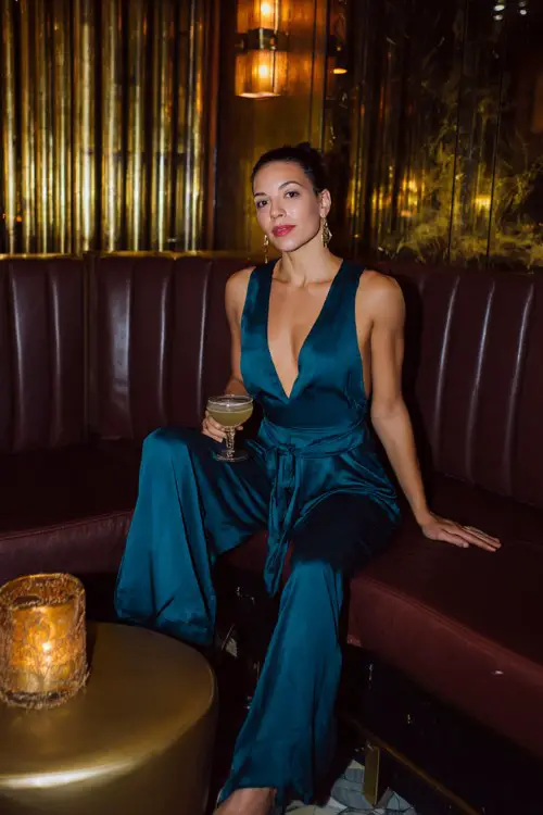 A woman over 30 wears a jewel-toned satin jumpsuit with wide legs and a plunging neckline