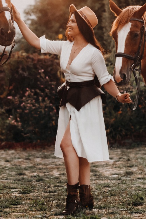 A woman wears cowboy boots with a white dress and a cowboy hat