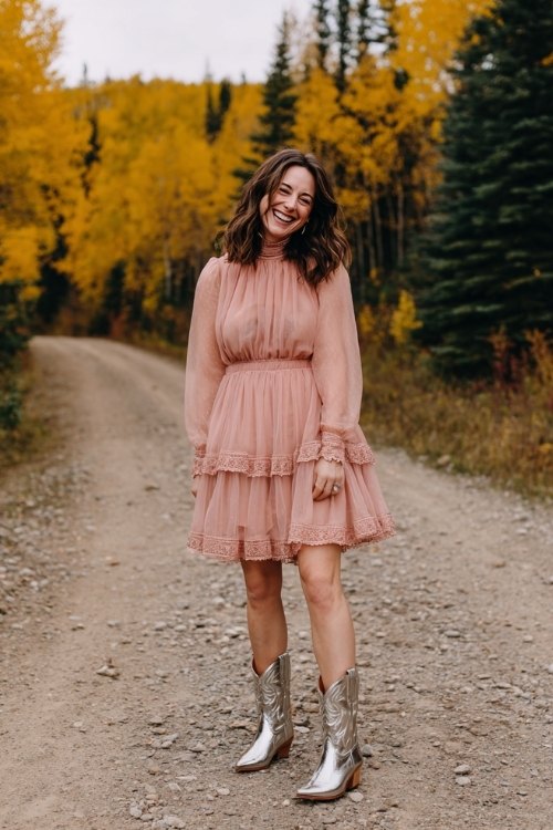 A woman over 30 wearing a blush pink A-line dress with a tiered sheer skirt and high neck, paired with metallic silver cowboy boots