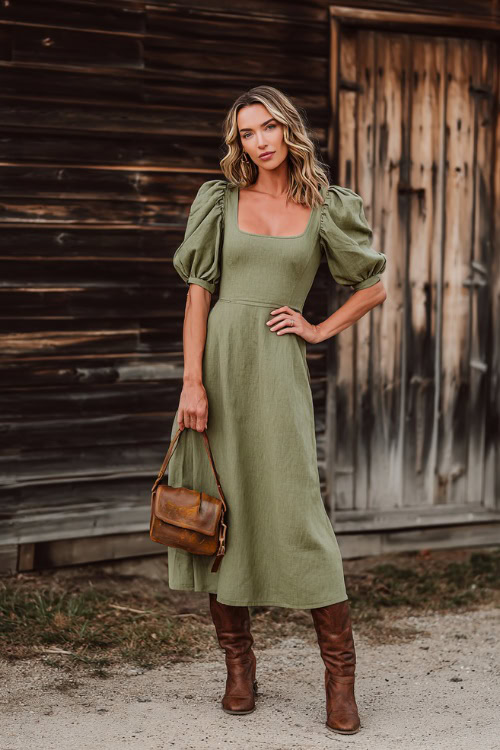 A woman wears a moss green midi dress with puff sleeves and a square neckline, styled with brown boots and a leather crossbody bag