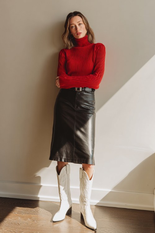 A woman in her 30s wears a fitted red turtleneck sweater, black faux leather skirt, and white cowboy boots (3)