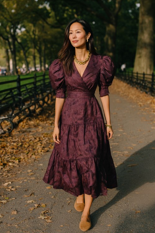 A woman wears a deep plum midi dress with puff sleeves, a tiered skirt, and vintage-inspired floral patterns