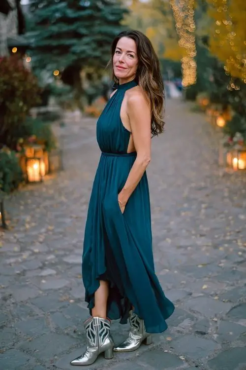 A woman over 40 in a dark teal chiffon maxi dress with a high neckline and keyhole back, paired with metallic silver cowboy boots