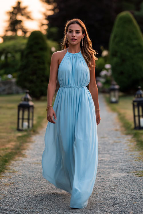 A woman in a soft sky blue flowy maxi dress with a halter neckline and delicate earrings, walking down a garden path lined with lanterns at a sunset wedding