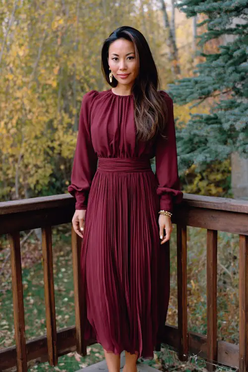 A woman over 30 wears a maroon chiffon pleated dress with cuffed long sleeves, styled with pointed-toe heels and pearl studs
