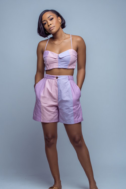 A Black woman in a matching pastel co-ord set with a crop top and high-waisted shorts, paired with slides and minimal jewelry, styled for a cute and casual summer going-out look