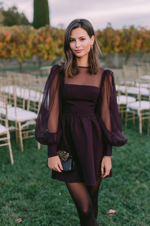 A petite woman in a deep plum A-line dress with sheer balloon sleeves and black tights, holding a small clutch