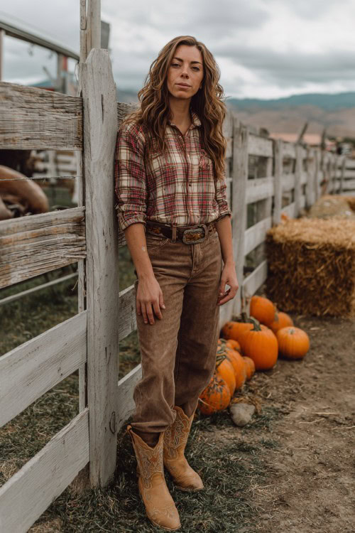 A woman over 30 wears bootcut jeans, a plaid button-up shirt tucked in, and tan suede cowboy boots