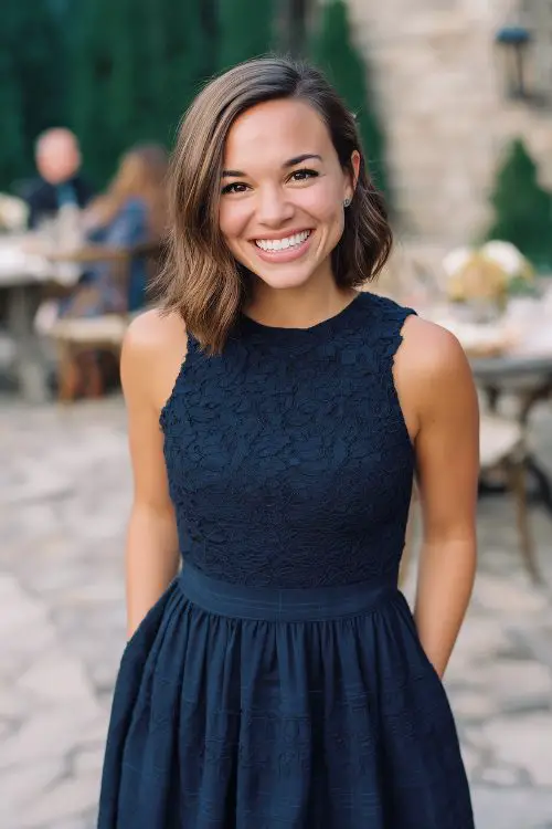 A petite woman wears a navy fit-and-flare dress with tiered lace and a subtle plaid overlay