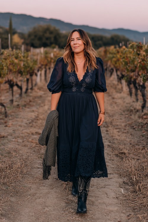 A curvy woman over 40 wears a navy chiffon maxi dress with sheer bishop sleeves and embroidered details, paired with black cowboy boots