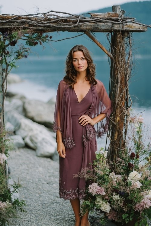 A petite woman in a dark mauve dress with a sheer cape-like overlay and embroidered flowers along the hem