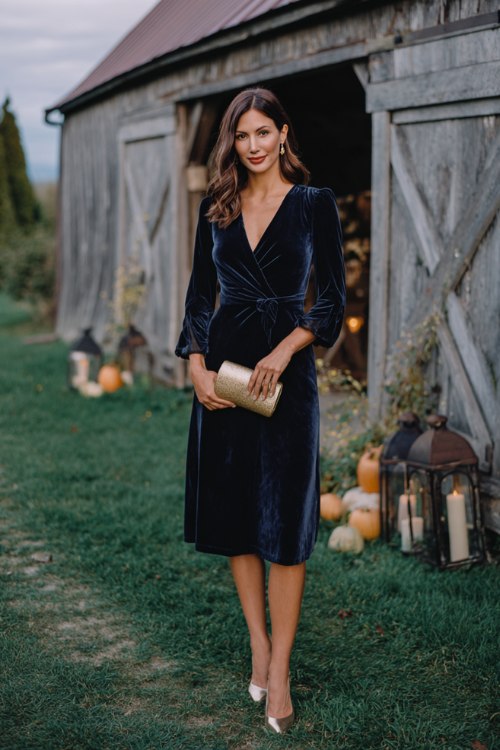 A woman wears a navy velvet wrap dress with sheer long sleeves, styled with metallic heels and a clutch (2)