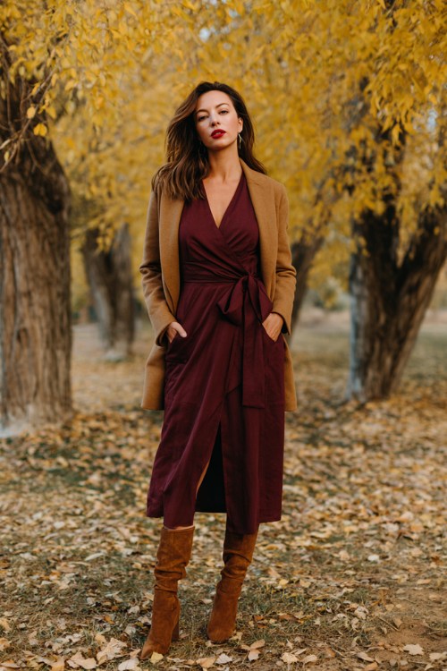 A woman over 30 wears a deep burgundy wrap dress with long sleeves, suede heeled boots, and a camel wool coat