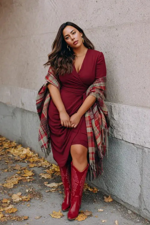 A curvy woman wears red cowboy boots, a burgundy wrap dress, and a plaid shawl