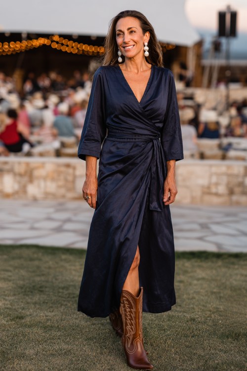 A woman over 40 wears a navy wrap maxi dress with long sleeves, accessorized with sleek brown cowboy boots and pearl earrings