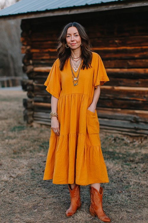 A woman over 30 wears a marigold tiered midi dress with flutter sleeves and short caramel cowboy boots