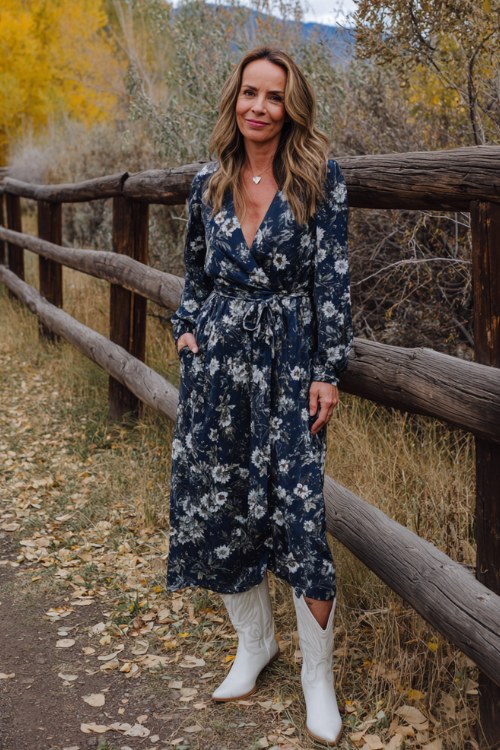 A woman over 40 wears a navy floral maxi dress with a belted waist, styled with white cowboy boots