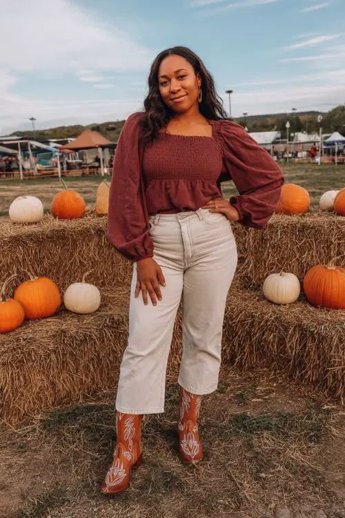 A curvy woman wears mid-rise jeans, a wine-colored bell-sleeve top, and brown cowboy boots with white stitching