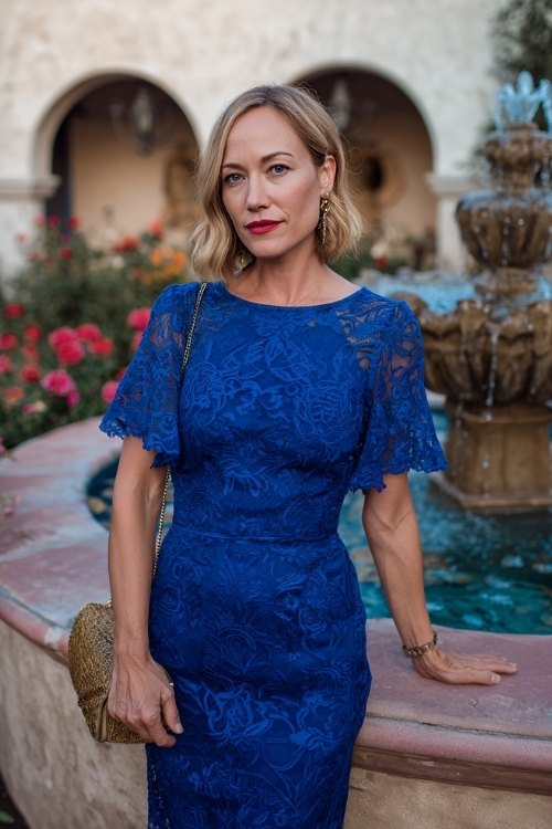 a woman over 50 in a royal blue lace overlay cocktail dress with flutter sleeves