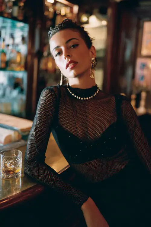 A woman wears a black mesh long-sleeve top over a crystal-embellished bra