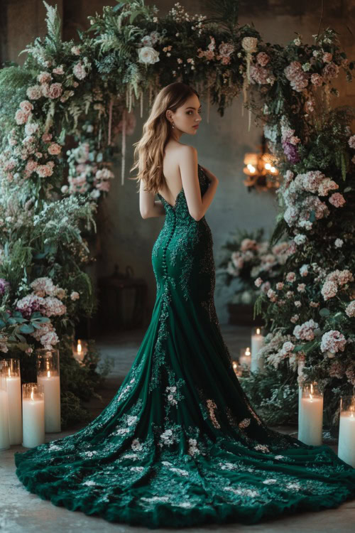 A woman in a deep emerald green mermaid gown with a sweetheart neckline, floral lace appliqueÌs, and a long flowing train