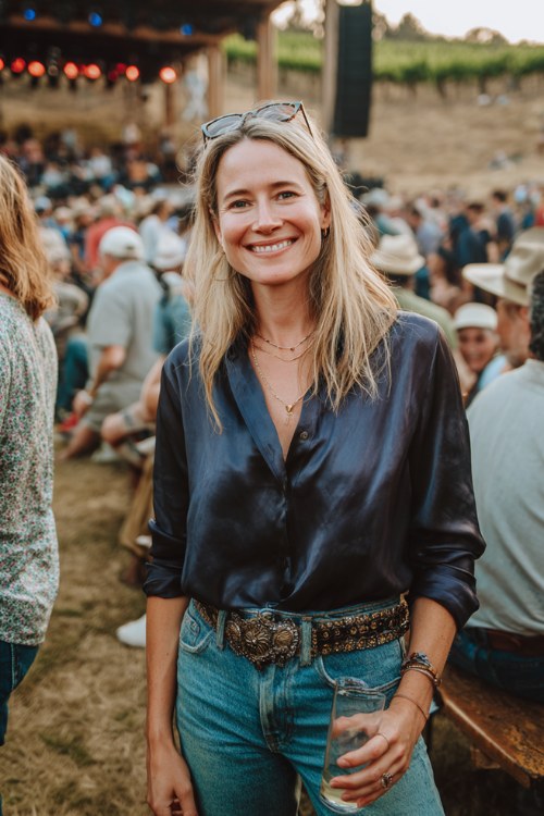 A woman over 30 wears straight-leg jeans with a silky navy blouse tucked in, paired with dark cowboy boots and a statement belt (2)