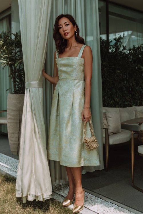 A woman over 40 wears a pale green jacquard A-line dress with a square neckline and thick straps