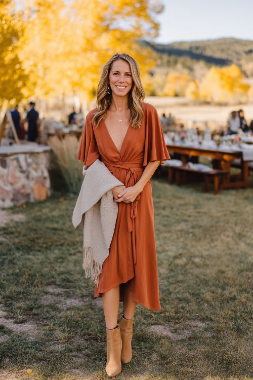 A stylish woman over 50 in a burnt orange midi dress with flutter sleeves and a flowy silhouette, paired with tan block-heeled boots and a light wool shawl (2)