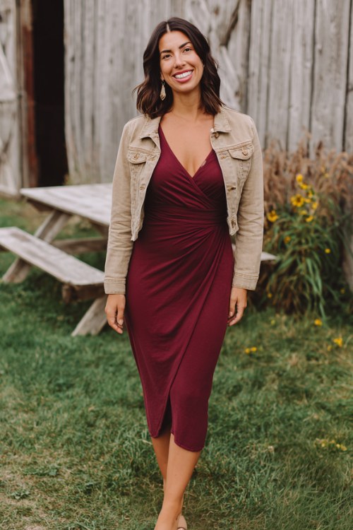 A woman wears a burgundy wrap midi dress with long sleeves, paired with a light-wash jean jacket and tan block heels