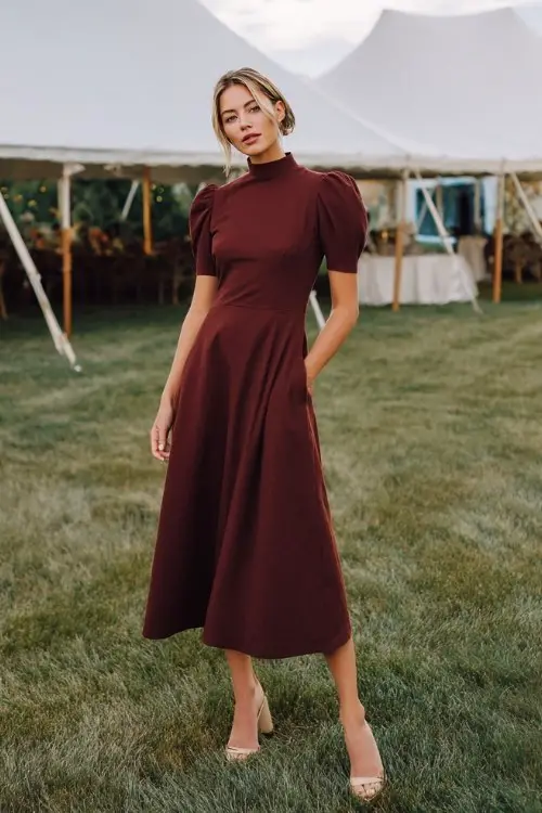 A woman wears a simple maroon high-neck dress with short sleeves, styled with low block heels