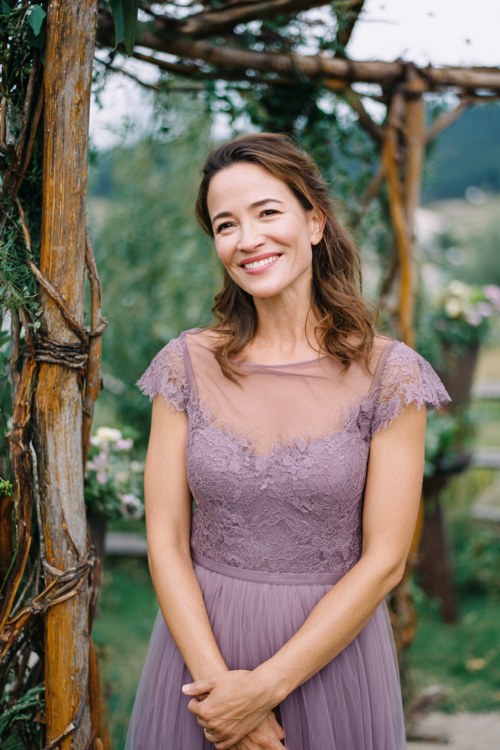 A woman over 50 wears a lavender midi dress with lace cap sleeves and a tulle skirt