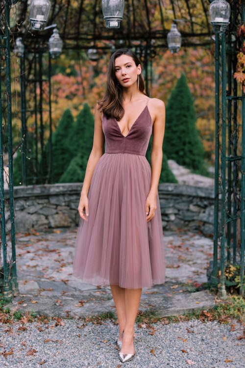A woman wears a mauve midi cocktail dress with a fitted bodice and tulle overlay skirt, finished with silver ankle-strap heel