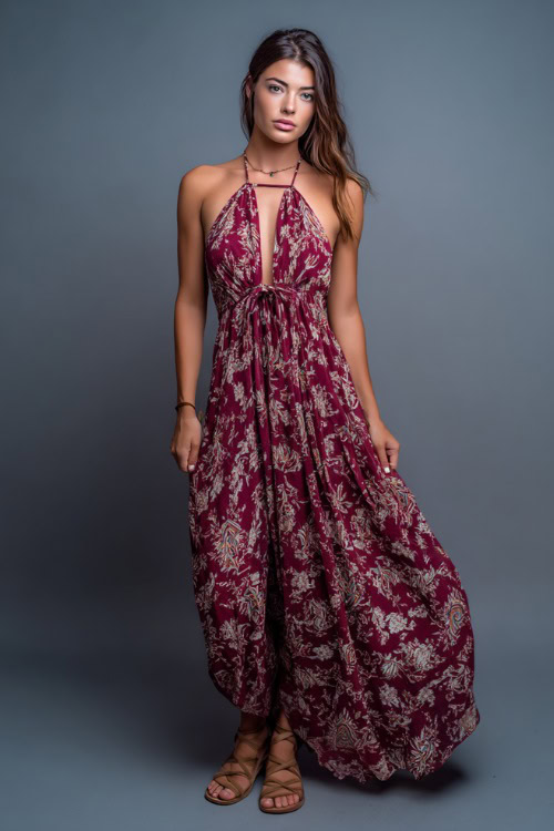 A woman in a flowy halter maxi dress with a low back and flat sandals, styled for a boho-inspired summer bar night, simple studio background