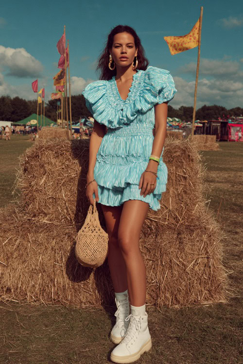A woman wearing a ruffled mini dress with puff sleeves and white platform sneakers, accessorized with hoop earrings and a woven handbag