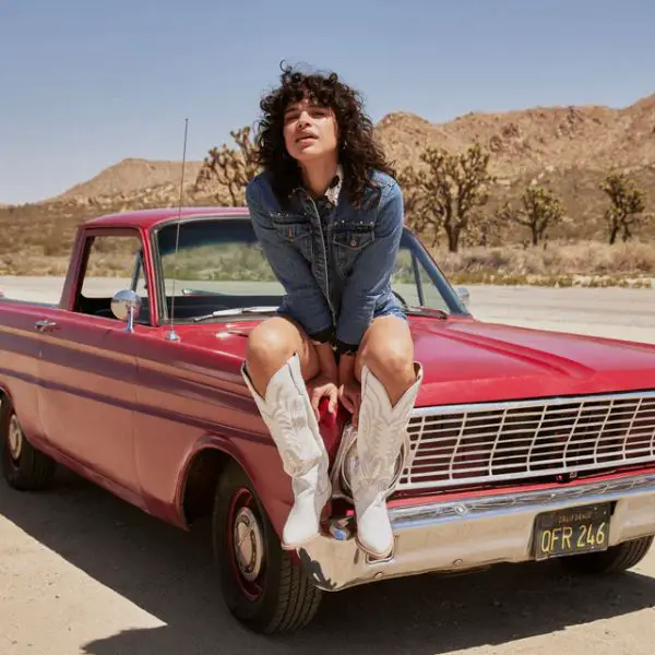 A woman wears denim shorts with denim jackets and a pair of knee high cowboy boots